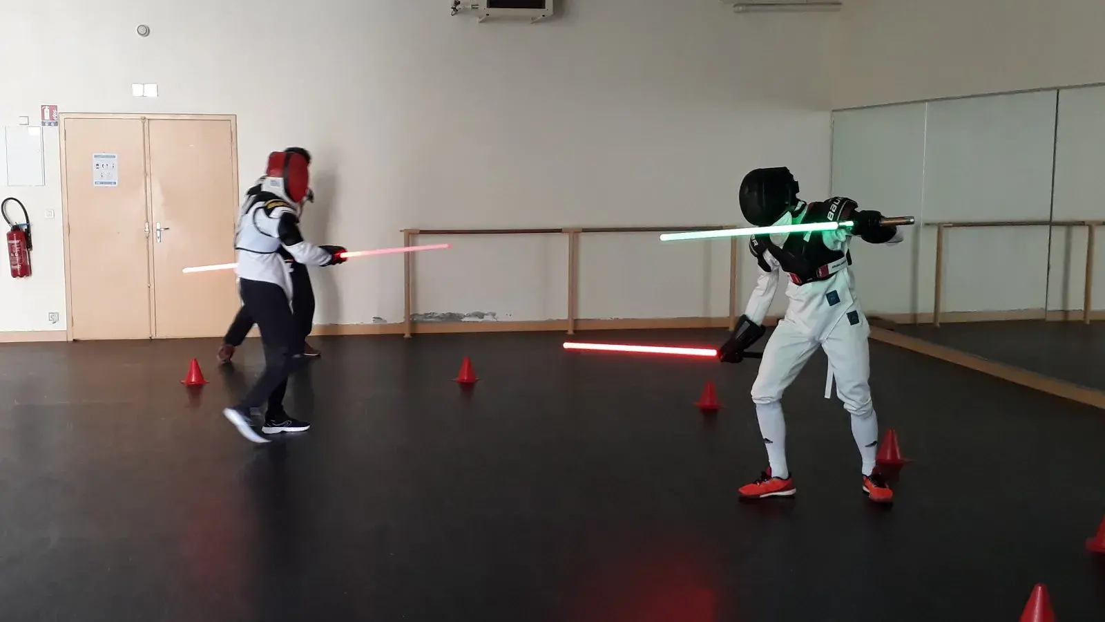 Duel de sabre laser, lames verte et rouge croisées en salle.